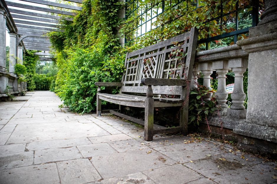 A neatly maintained garden featuring a lush, green lawn bordered by well-trimmed hedges and a variety of flowering plants. In the foreground, a gardener's tools such as pruning shears and a rake are v